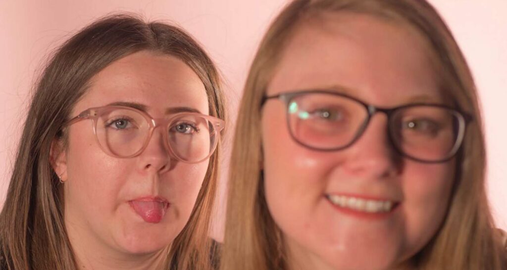 two women students in glasses, one sticking out tongue