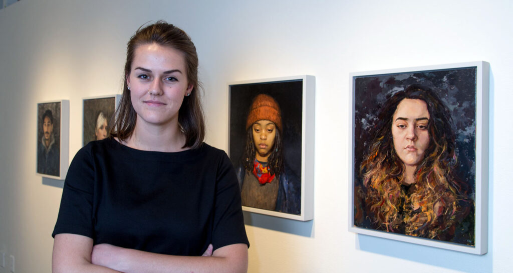 woman standing next to portrait paintings