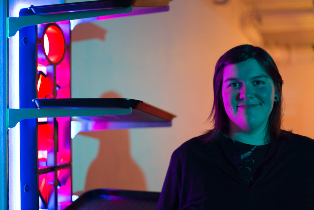 student posing next to neon sculpture with meal trays