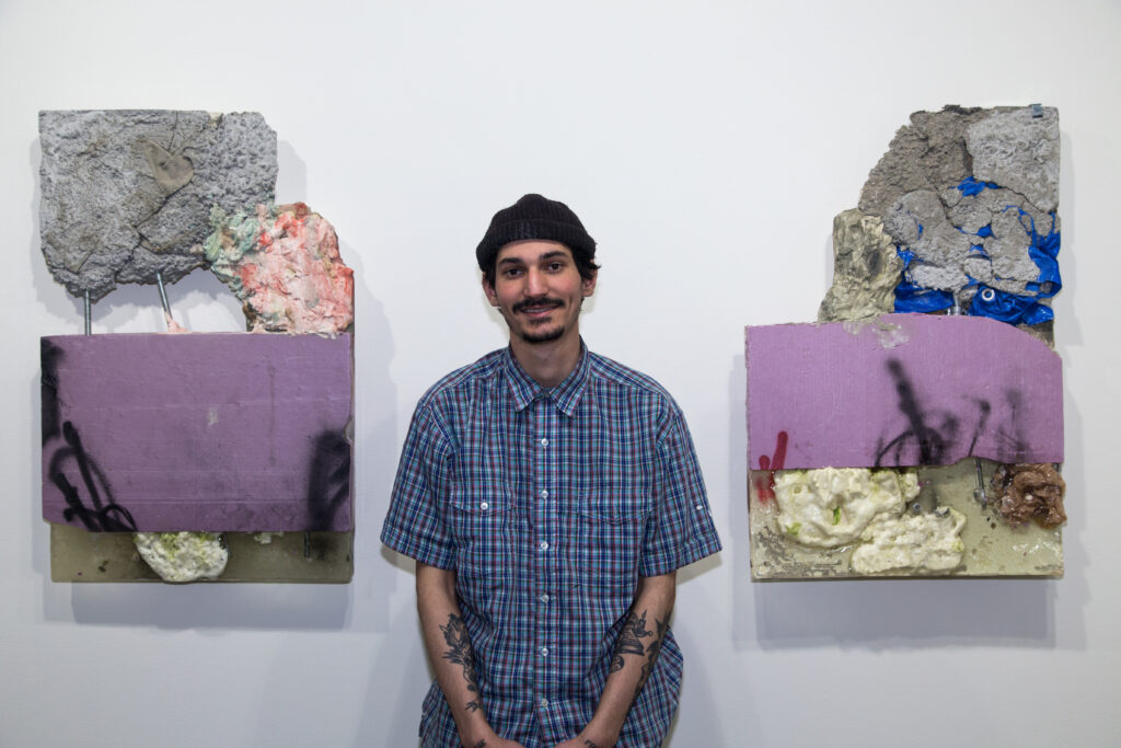 student posing next to sculptures made of insulation and construction materials