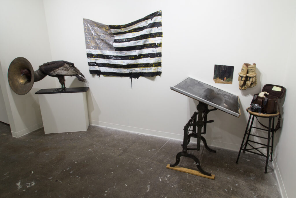 black and white sculpture of bird, old style record player, desk , and American flag in gallery