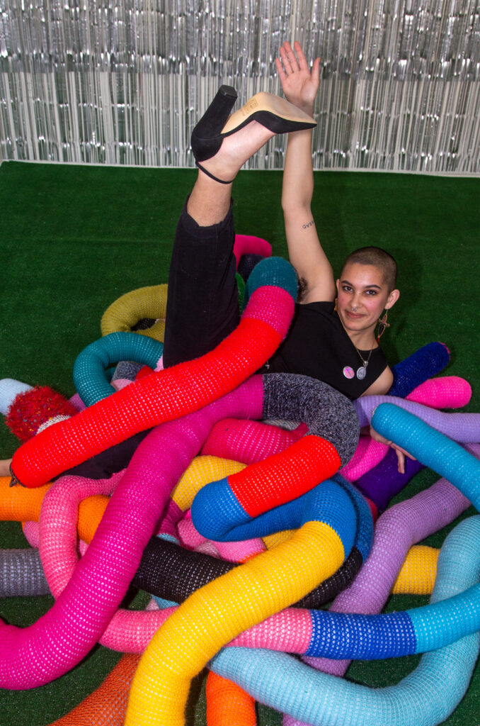 artist laying on soft sculptures of worms with leg in the air