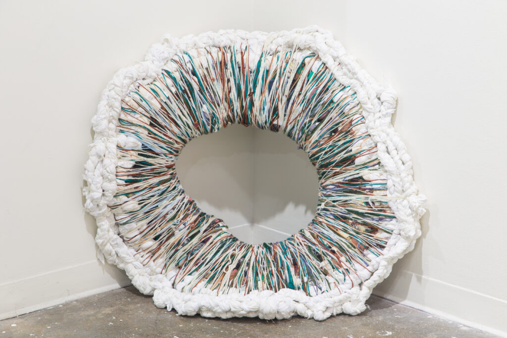 round textile sculpture with hole in the middle leaning against corner of wall