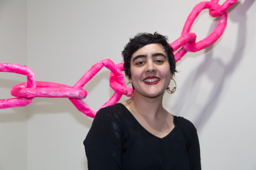 student smiling in front of large pink chain sculpture