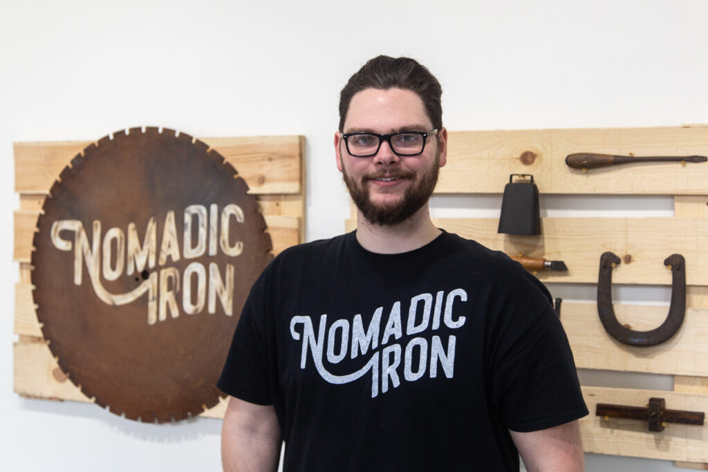 man standing in front of branded vintage hand tools reading "nomadic iron"