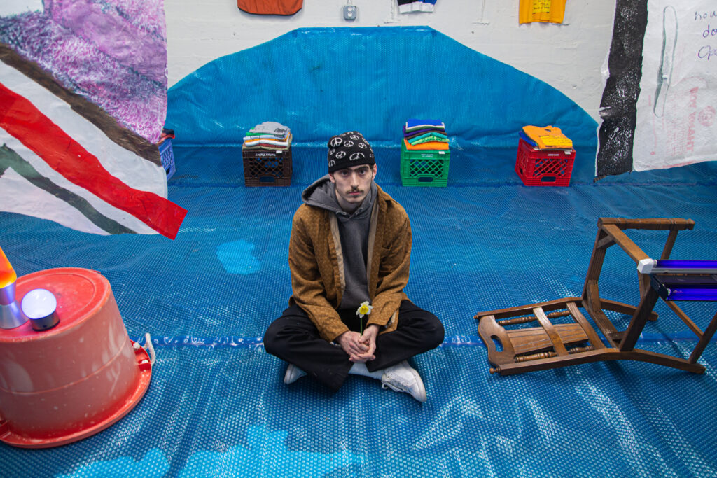 portrait of artist sitting on pool cover with art around him