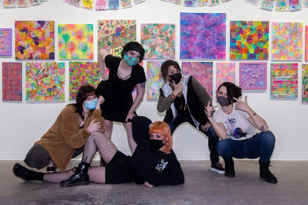 five women posing in front of paintings with masks on