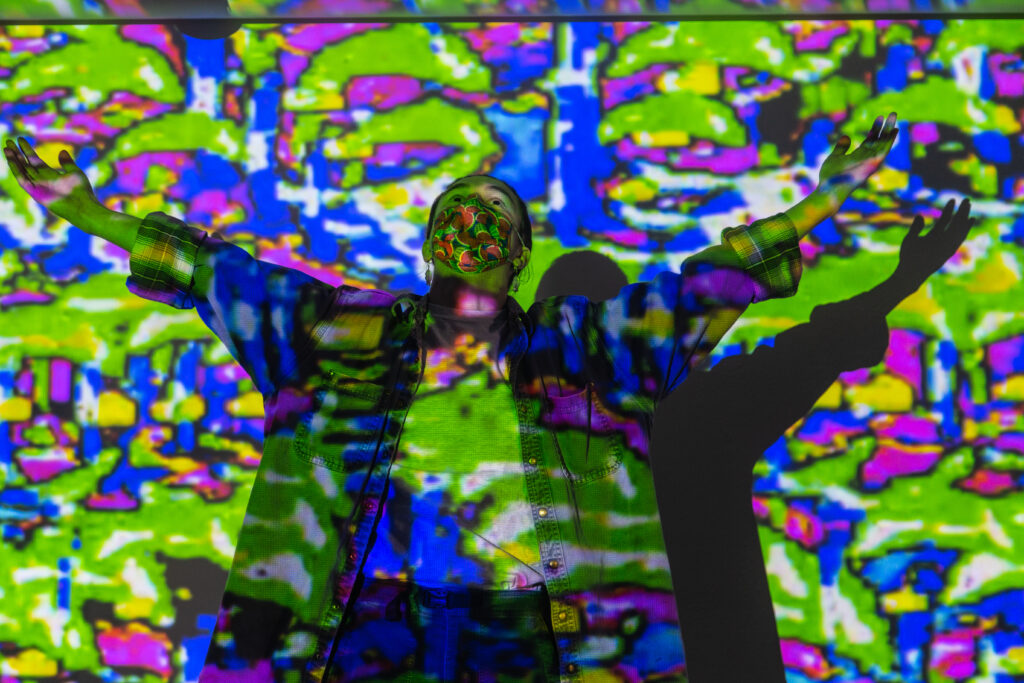 student posing with arms spread in front of wall projected with colorful digital pattern