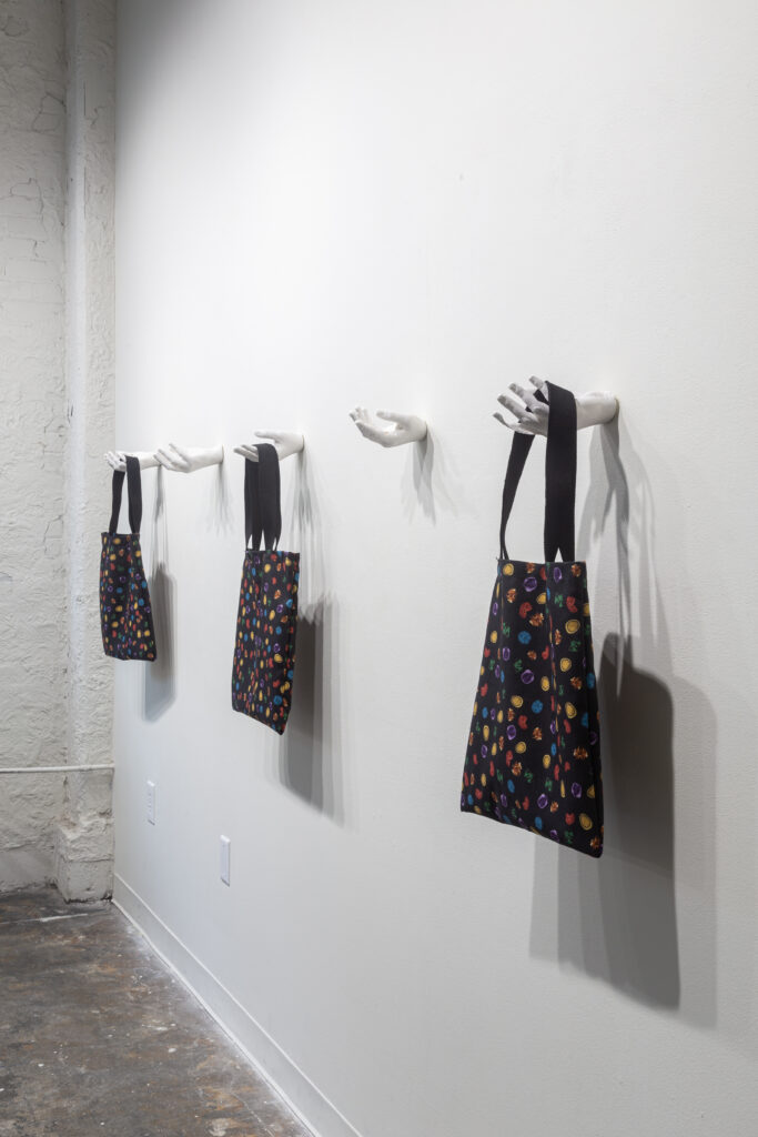black tote bags with colorful patterns hanging from white hand sculptures suspended on wall