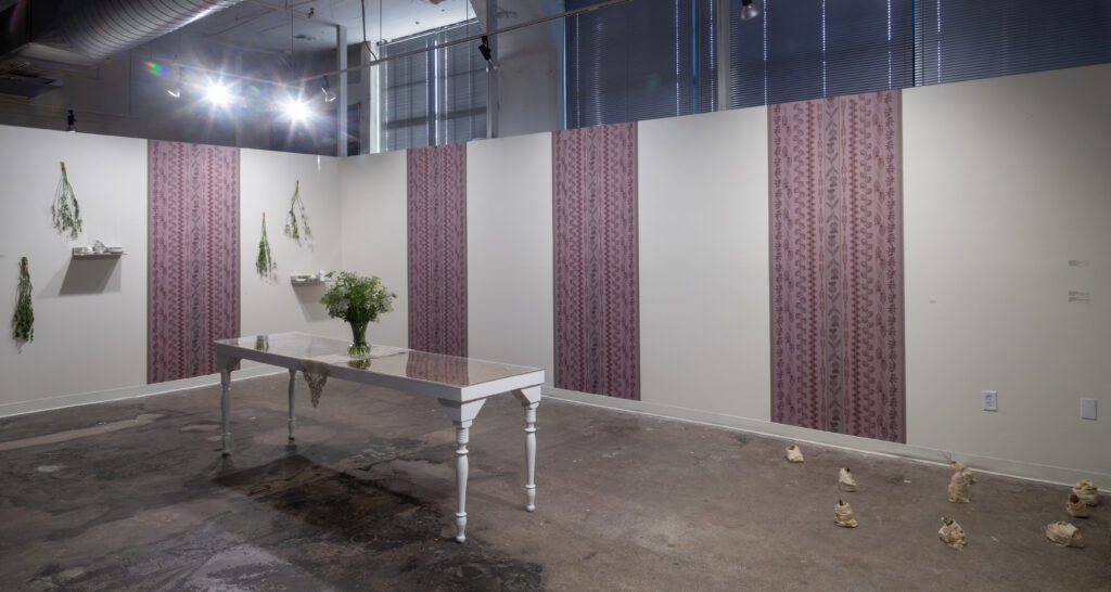 installation of dining table with plant in front of strips of patterned wallpaper and hanging plants