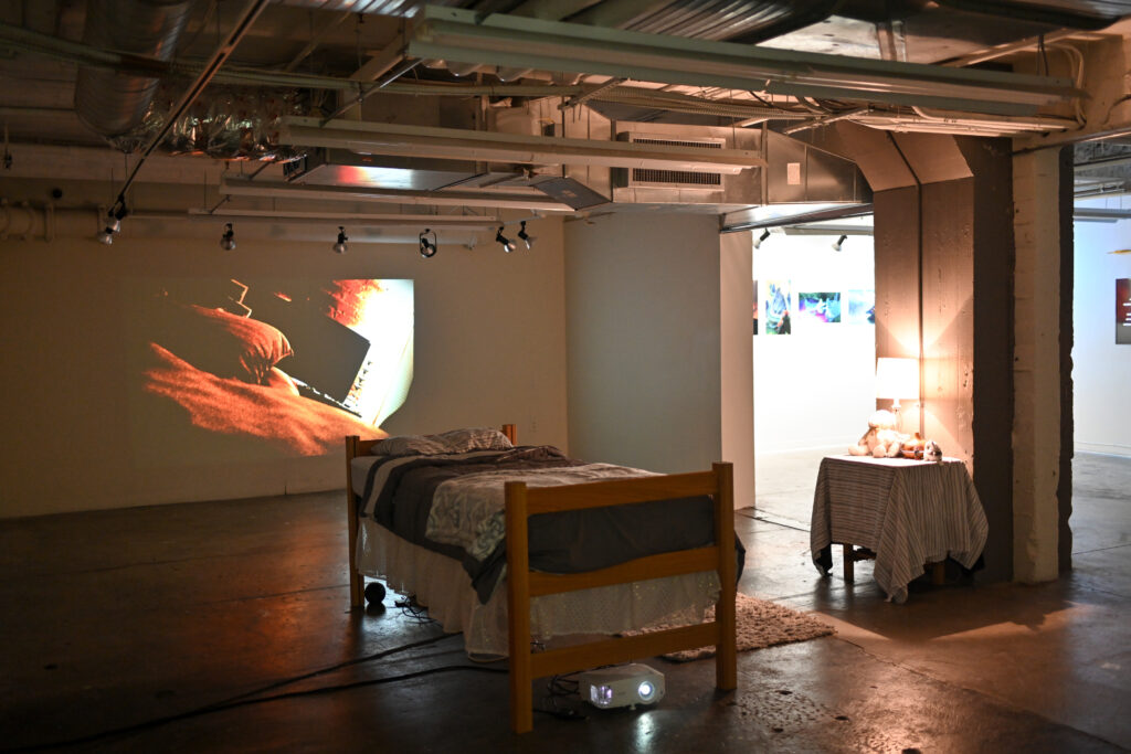 gallery installation of bed in front of projected image of a bed