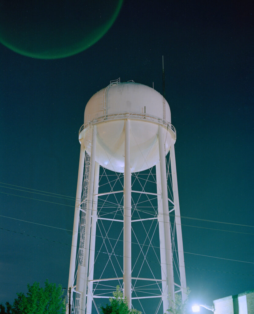 white water tower in front of blue-green night sky