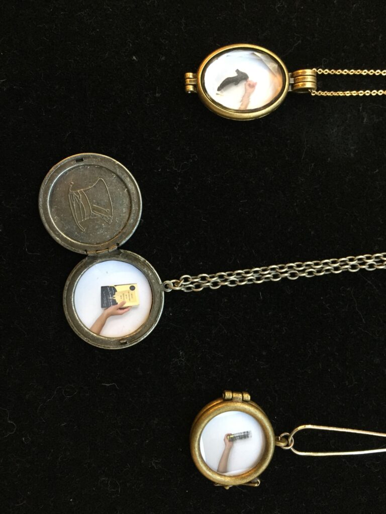 three lockets containing images of hands holding shoe, book, and glass