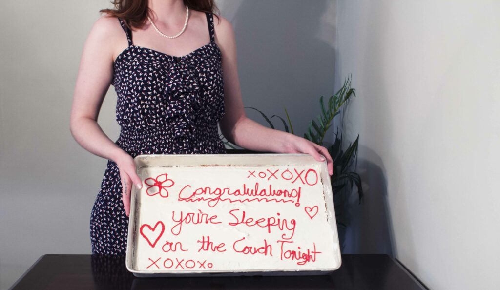 neck-down shot of woman holding cake with icing reading "congratulations! you're sleeping on the couch tonight"