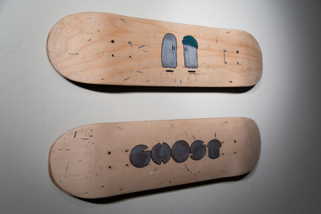 two wall-mounted wood skate decks painted with simple ghost illustrations and the word "ghost" in thick stylized font