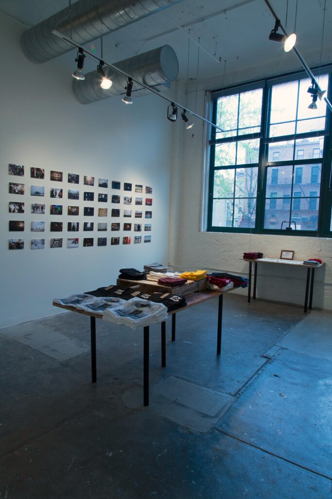 gallery installation of table with t shirts, and wall of photos