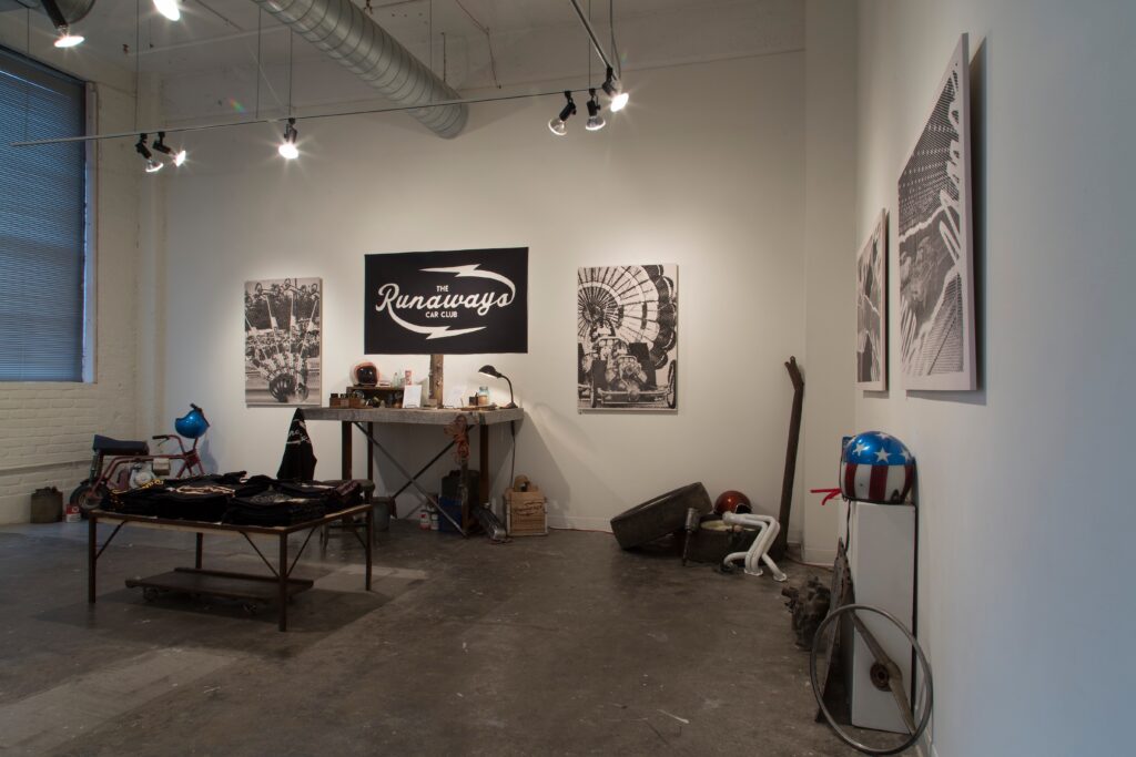 installation with hanging prints and tables of t-shirts and various equipment and supplies