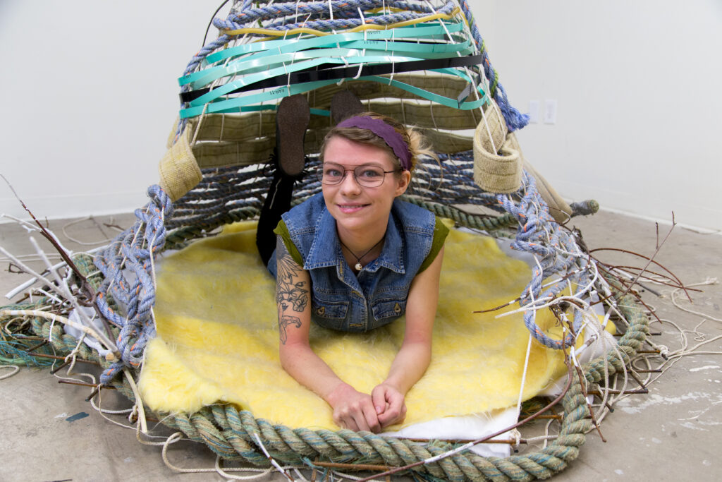 woman laying inside of rope and textile nest sculpture