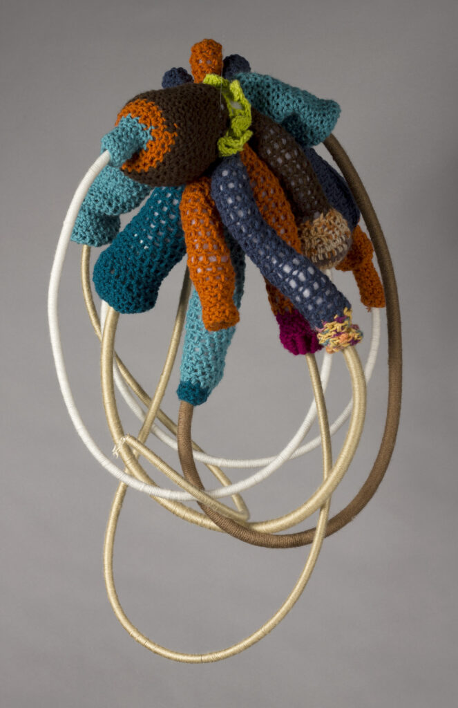 hanging sculpture made up of bundle of stuffed knit phallic shapes with ropes emerging from ends