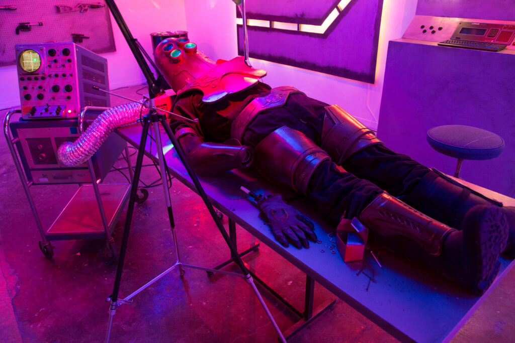 installation of life-size robot sculpture lying on table surrounded by tools and equipment