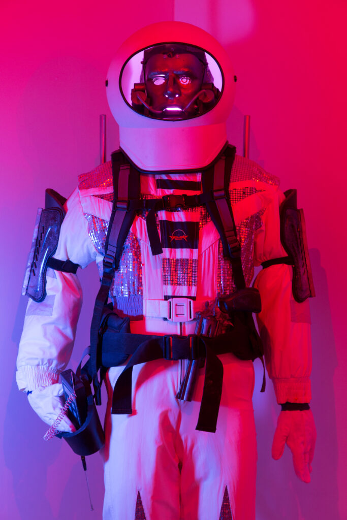 sculpture of figure in space suit lit in red and blue