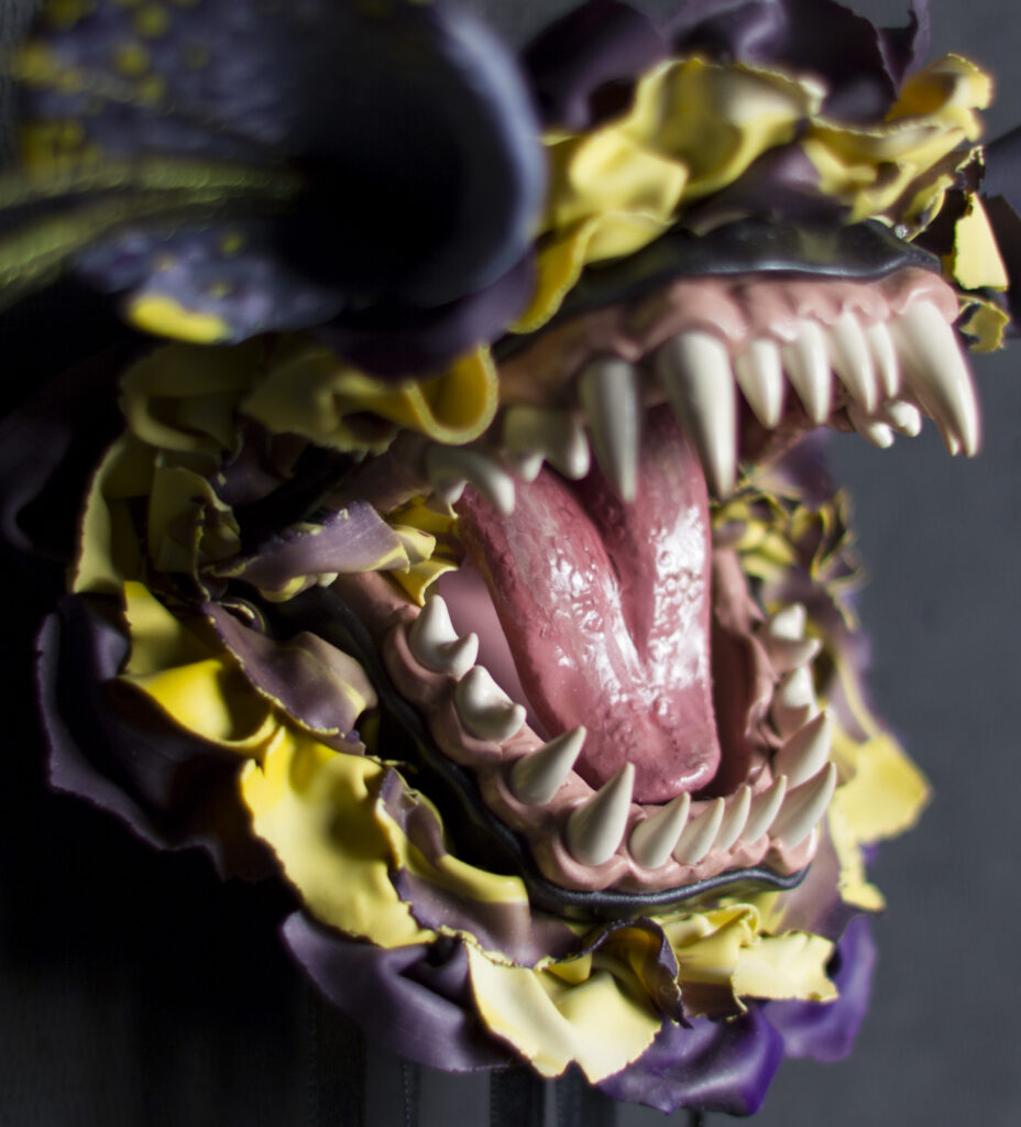 detail shot of sculpture of open mouth of fanged creature with skin resembling flower petals