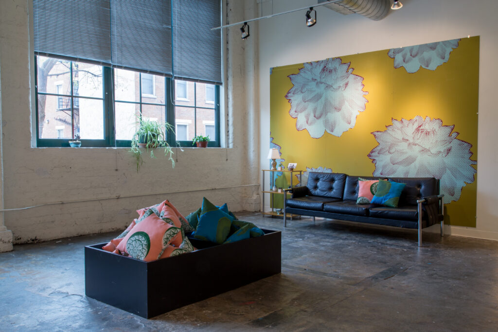 box with printed pillow and sofa in front of yellow floral wallpaper in gallery