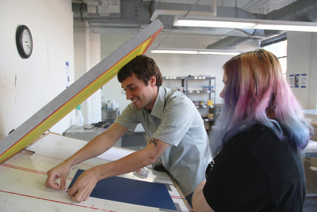 Teen academy student is screen printing with the instructor.