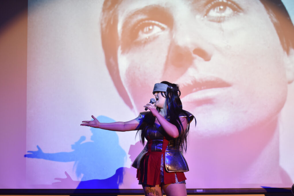 woman performing in costume in front of projection of woman's face