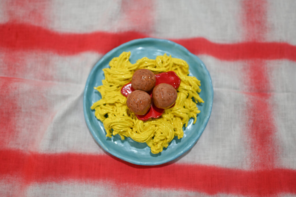 ceramic spaghetti and meatballs on blue plate on white fabric with red grid