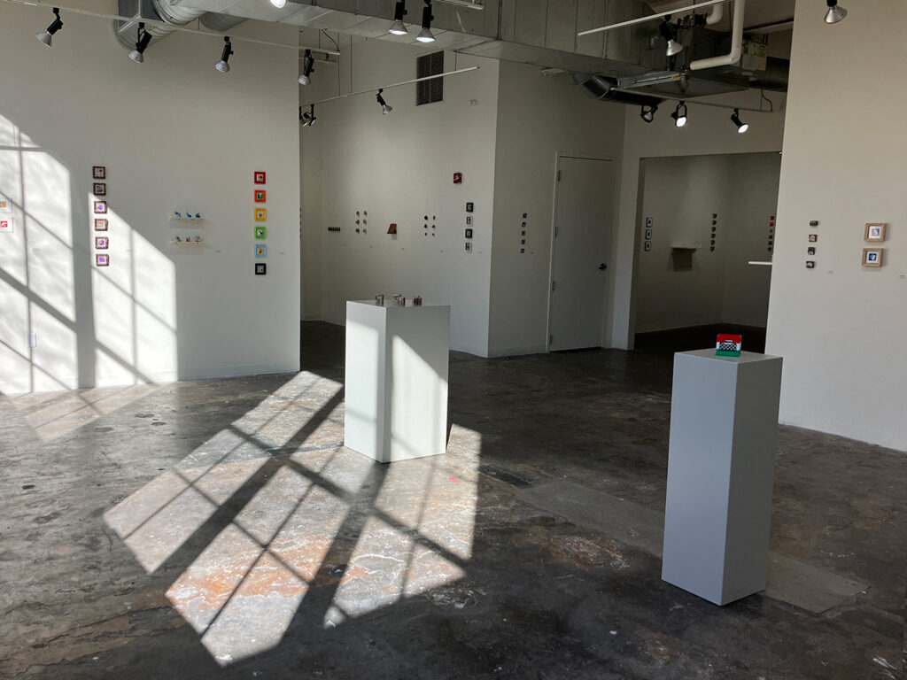 View of an art gallery with groups of small artworks hung on the walls