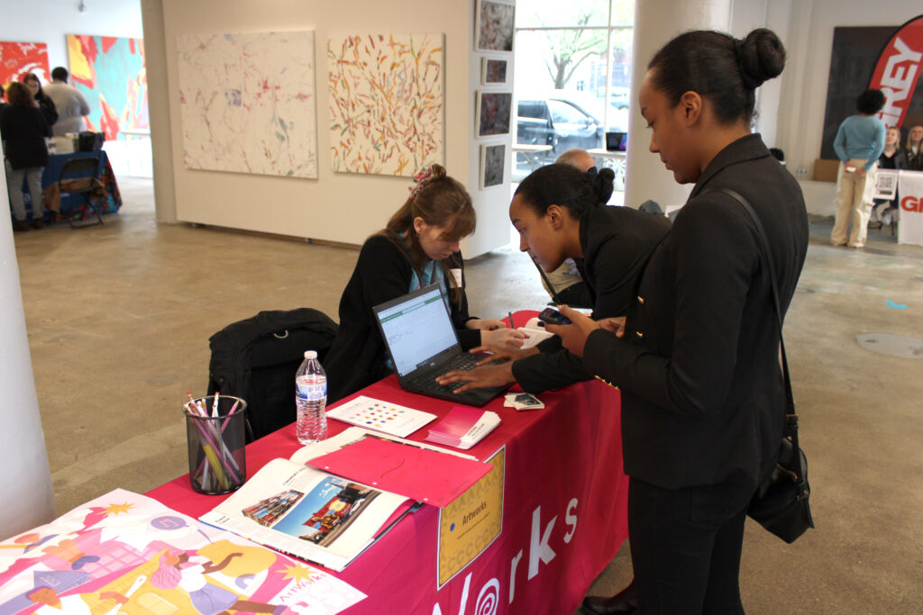 Two students fill out information forms for ArtWorks at the Spring 2023 Career Fair in SITE1212 at the Art Academy of Cincinnati.