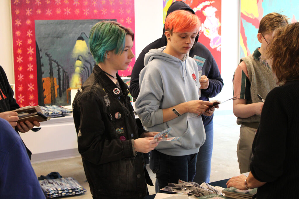 Two students getting information at from a prospective employer at the Spring 2023 Career Fair in SITE1212 at the Art Academy of Cincinnati.