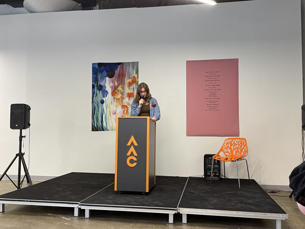 A student speaks at a podium during the Spring 2023 WAAC literary magazine Release Party in SITE1212 at the Art Academy of Cincinnati.
