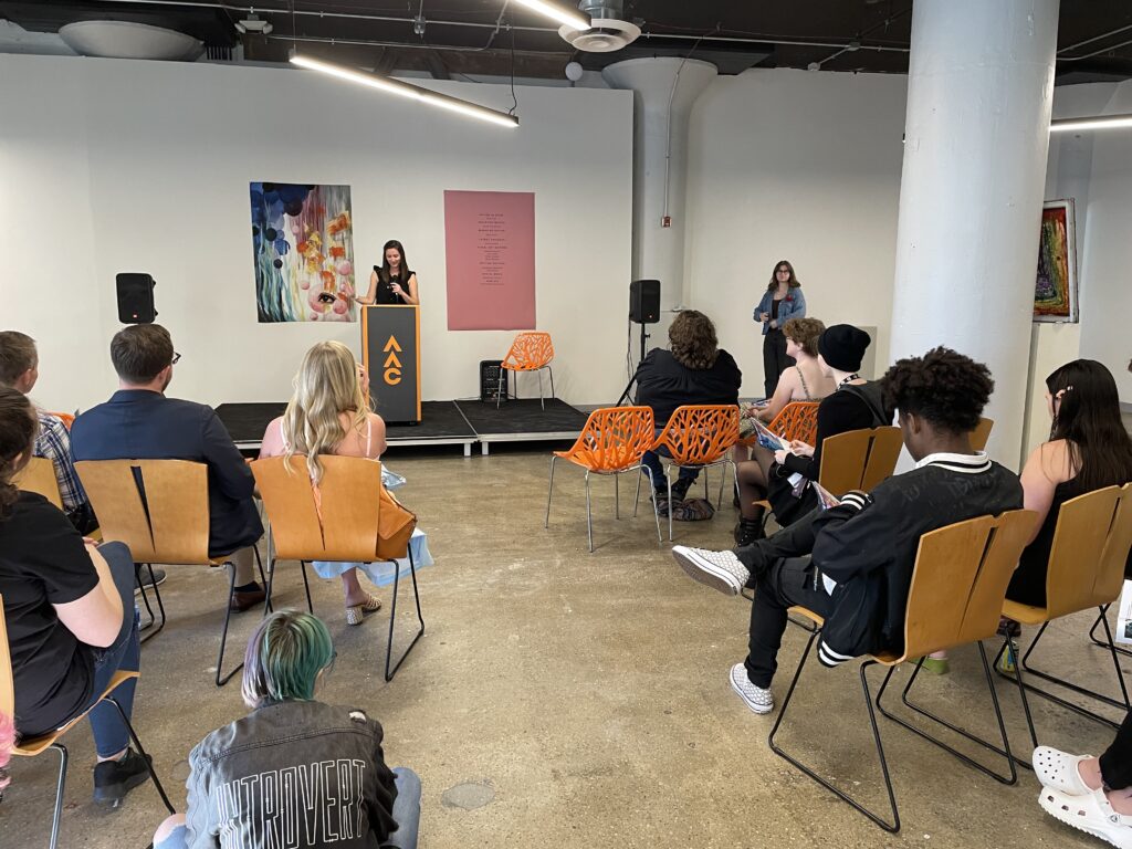 Attendees listen to a speaker at a podium during the Spring 2023 WAAC literary magazine Release Party in SITE1212 at the Art Academy of Cincinnati.