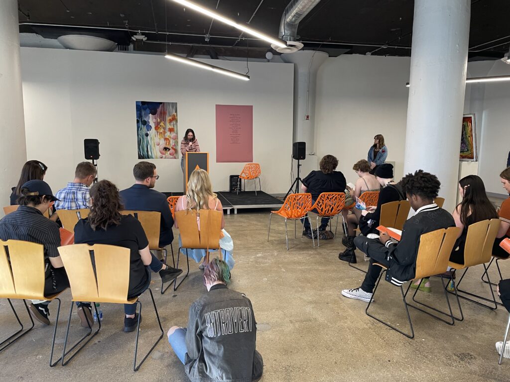 Attendees listen to a speaker at a podium during the Spring 2023 WAAC literary magazine Release Party in SITE1212 at the Art Academy of Cincinnati.