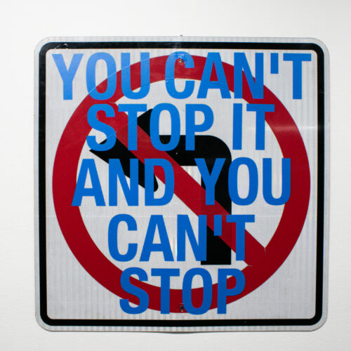 No left turn street sign with blue text over it saying "you can't stop it and you can't stop" by artist Cas Landman