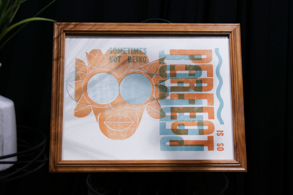 A framed screen print depicting a stylized face and the words "sometimes not being perfect is so perfect"