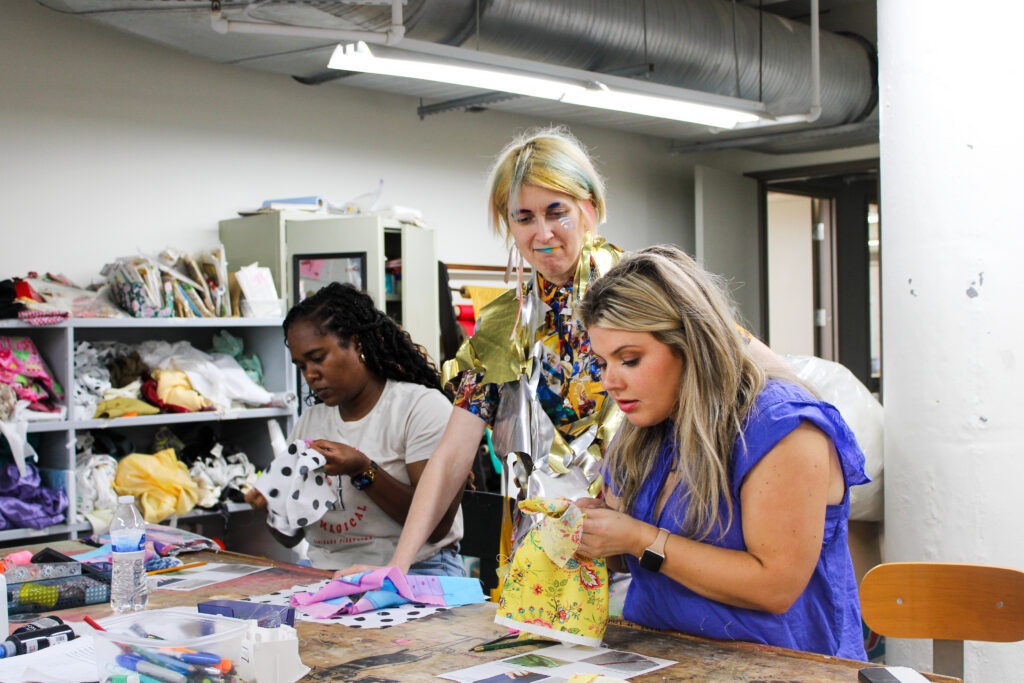 Woman in colorful clothing teaching two students in textiles lab