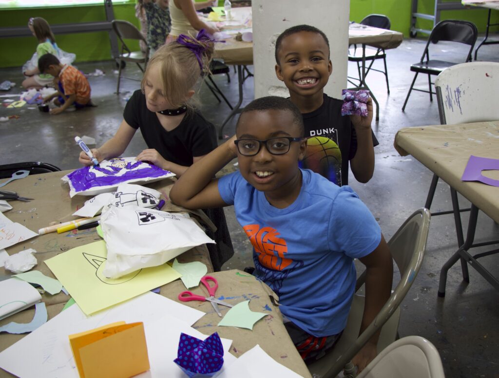 three children smiling and making art at a table
