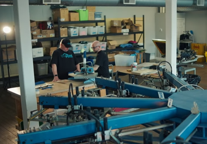 photo of a large screen printing machine with Aaron Broughton of Point Apparel in the background